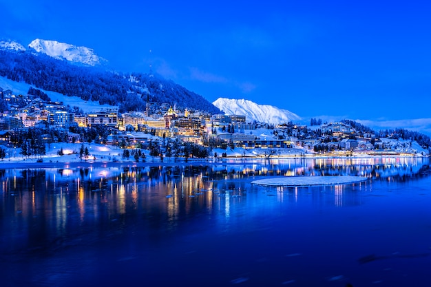 Vista das luzes da noite bonita da cidade de st. moritz na suíça à noite no inverno, com reflexo das montanhas do lago e da neve no backgrouind