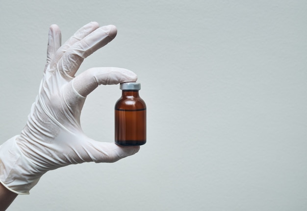 Vista das mãos da enfermeira com luvas, mostrando a ampola do medicamento com espaço de cópia.
