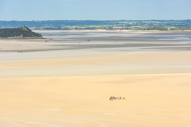 Vista das paredes do Mont Saint Michel na baía durante a maré baixa com grupos de turistas caminhando. França