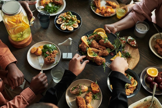 Vista de alto ângulo da família sentada à mesa de jantar e comendo frango juntos durante o evento de férias