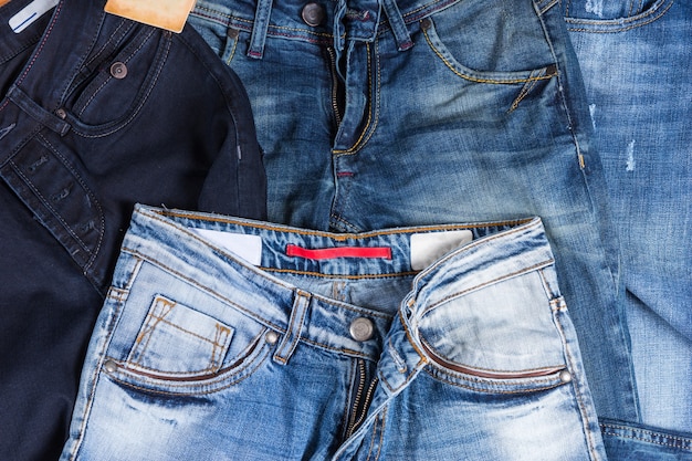 Vista de alto ângulo da pilha da frente da calça jeans em várias tonalidades de cores e estilos no fundo da superfície de madeira