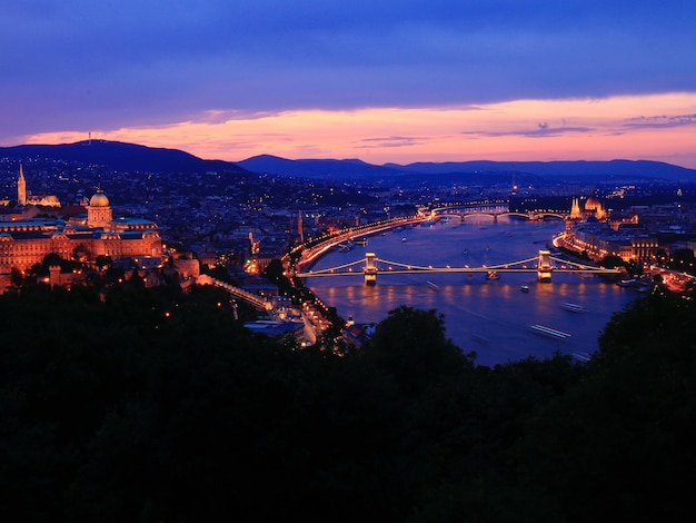 Vista de alto ângulo da ponte iluminada sobre o rio na cidade durante o pôr do sol