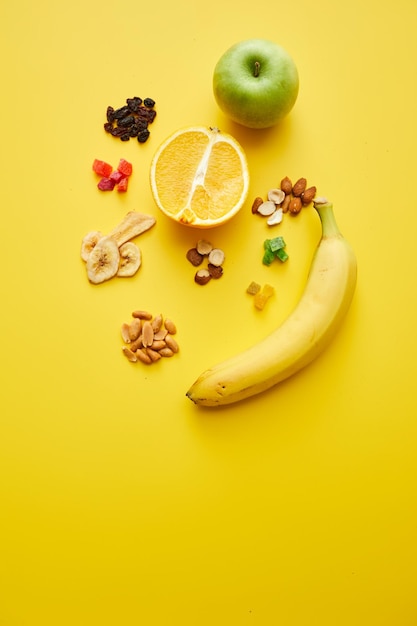 Vista de alto ângulo da seção transversal de frutas e nozes fritas de banana maçã laranja em fundo amarelo