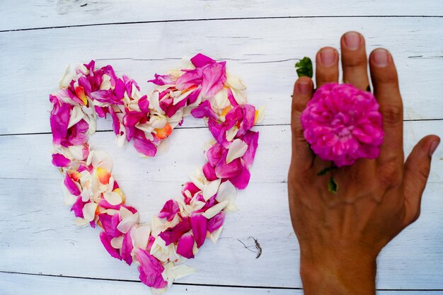 Foto vista de alto ângulo de forma de coração feita com pétalas por mão de homem segurando flor na mesa