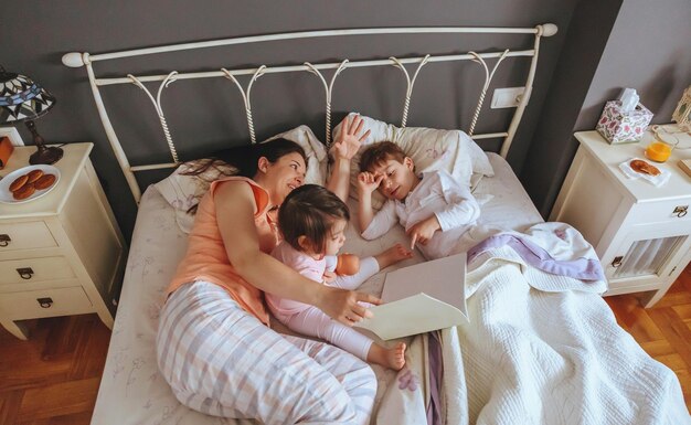 Vista de alto ângulo de mãe contando uma história para as crianças na cama em casa