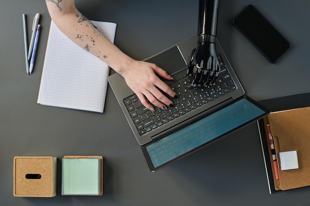 Vista de alto ângulo de mulher com braço protético digitando no laptop trabalhando online