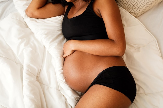 Vista de alto ângulo de mulher grávida vestindo roupa interior deitada na cama em casa