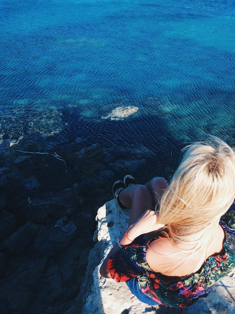 Foto vista de alto ângulo de mulher sentada em uma rocha ao lado do mar