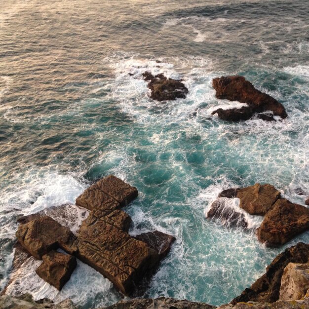 Foto vista de alto ângulo de ondas espalhando-se sobre rochas no mar