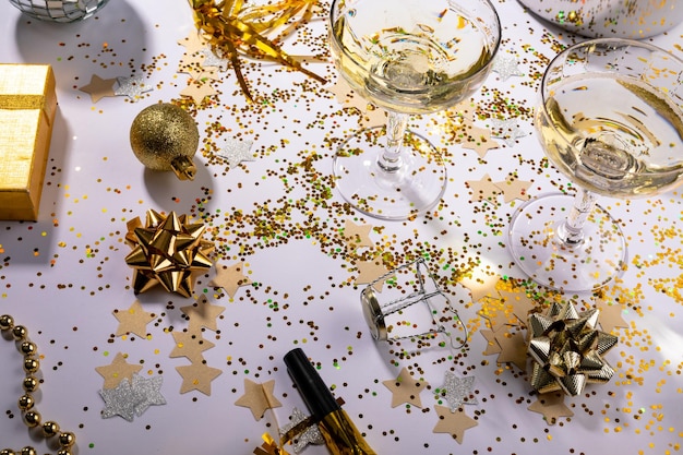 Vista de alto ângulo de taças de champanhe em confetes espalhados com presente e decoração na mesa. celebração de Natal e festa com espaço de cópia.