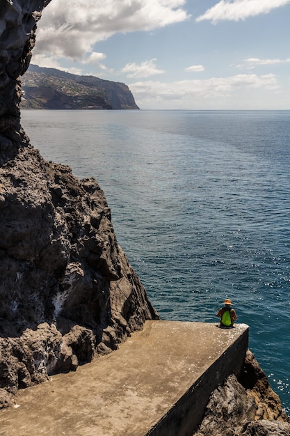 Foto vista de alto ângulo de um homem sentado em um penhasco contra o mar