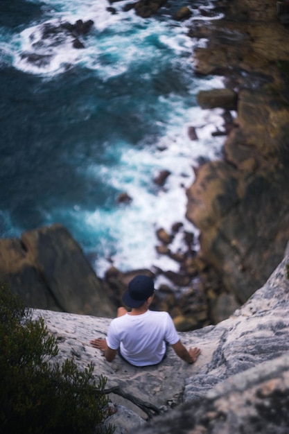 Vista de alto ângulo de um homem sentado na borda da rocha sobre o mar