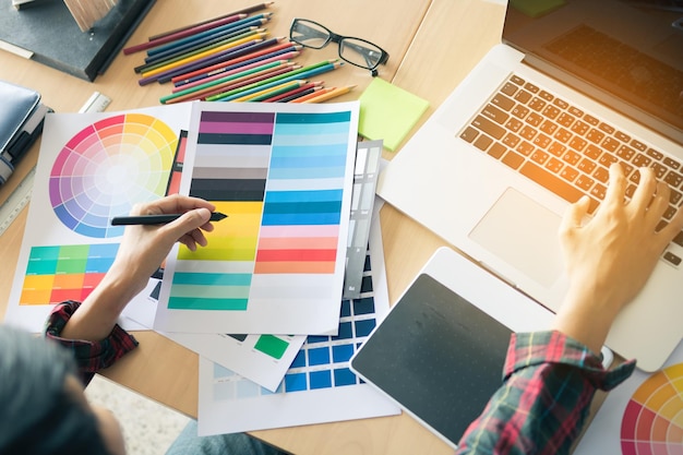 Foto vista de alto ângulo de um homem trabalhando em amostras de cores enquanto usa um laptop