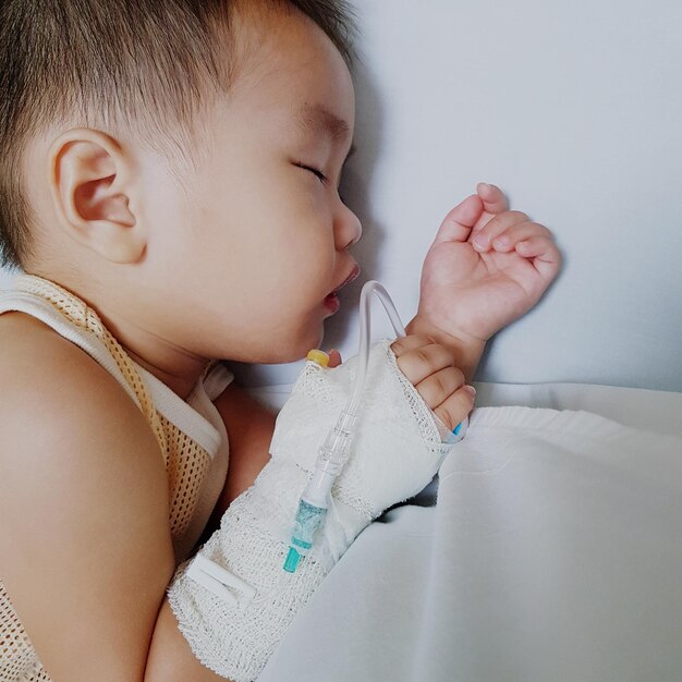 Foto vista de alto ângulo de um menino bebê com gotejamento intravenoso dormindo em uma cama no hospital