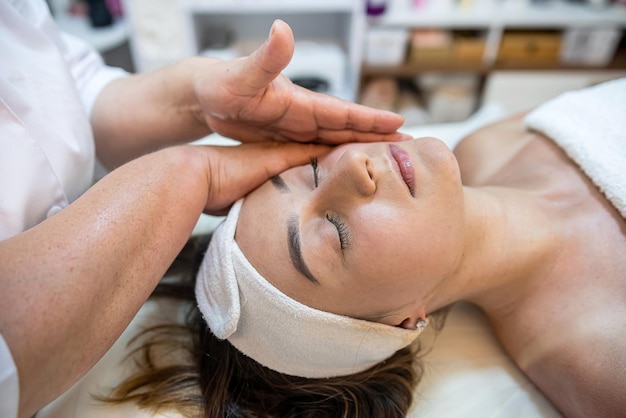 Vista de alto ângulo do massoterapeuta massageando o rosto de uma cliente morena com os olhos fechados