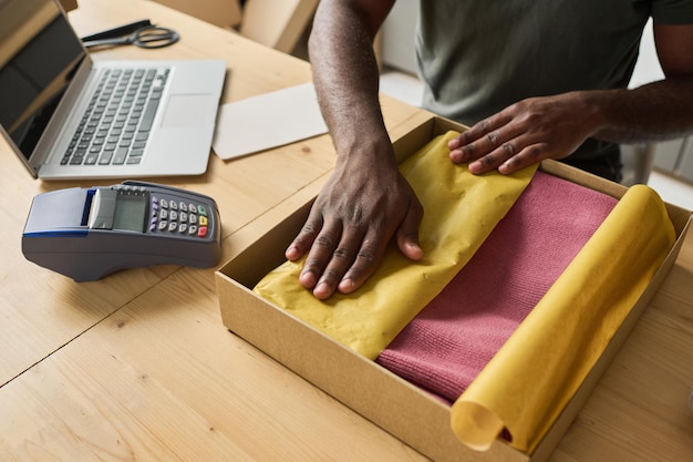 Vista de alto ângulo do trabalhador embalando roupas novas em caixa de papelão na mesa para fazer encomendas para entrega