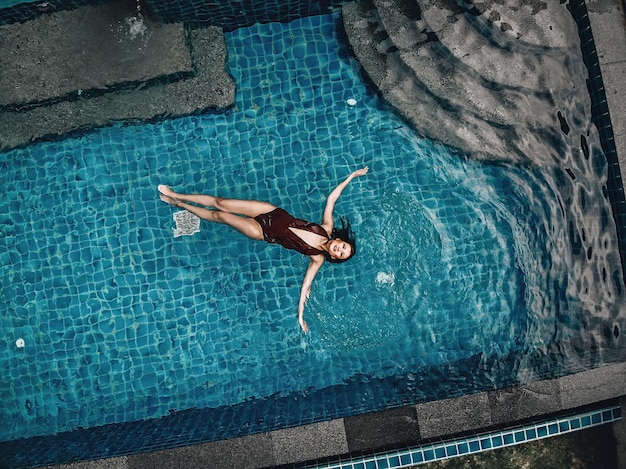 Vista de alto nível da bela jovem nadando na piscina azul; conceito de relaxamento.