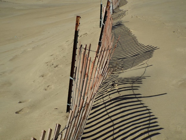 Vista de ângulo alto da sombra da cerca na areia durante o dia ensolarado