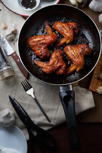 Vista de ângulo alto de asas de frango fritas na panela de cozinha na mesa