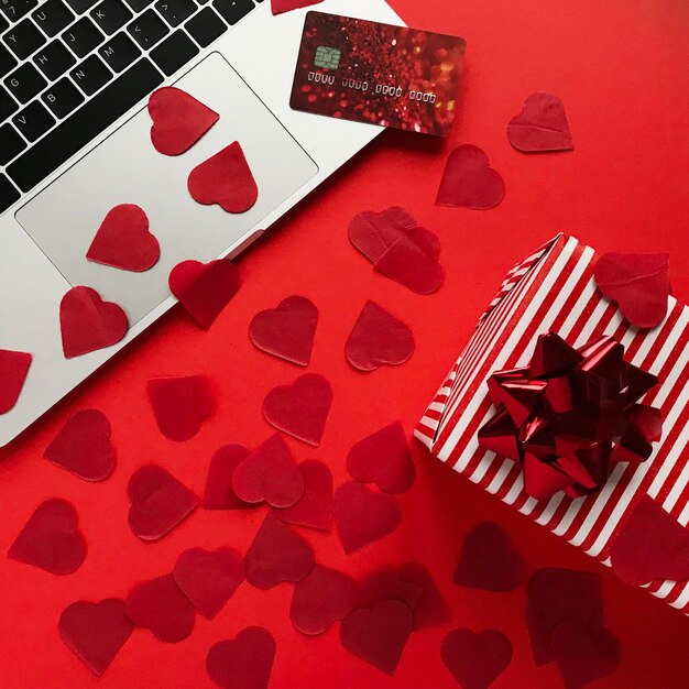 Foto vista de ângulo alto de cartão de crédito e laptop com confete sobre caixa de presentes em fundo vermelho