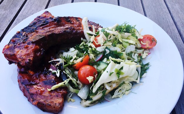 Foto vista de ângulo alto de costelas de porco grelhadas com salada servida em prato na mesa