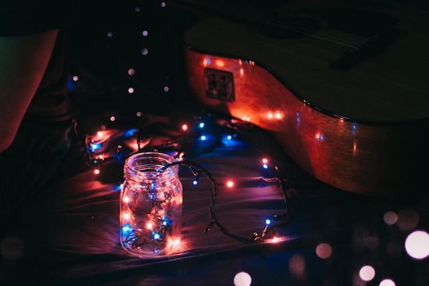Vista de ângulo alto de luzes de cordas iluminadas com frasco e guitarra na cama na sala escura