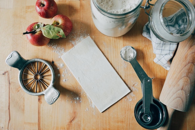 Foto vista de ângulo alto de maçãs com farinha e utensílios de cozinha em mesa de madeira