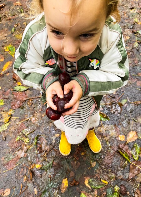 Foto vista de ângulo alto de menina bonita segurando frutas enquanto está de pé em terra