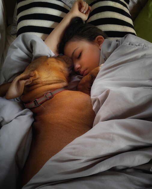 Foto vista de ângulo alto de menina com cachorro dormindo na cama em casa