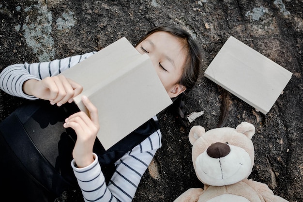 Vista de ângulo alto de menina com livro deitado por ursinho de pelúcia no campo