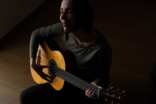 Foto vista de ângulo alto de mulher com os olhos fechados tocando guitarra enquanto está sentada em casa