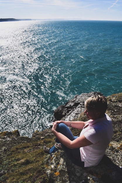 Vista de ângulo alto de mulher madura sentada em um penhasco ao lado do mar