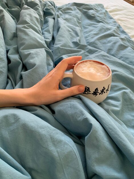 Foto vista de ângulo alto de mulher segurando xícara de café na cama