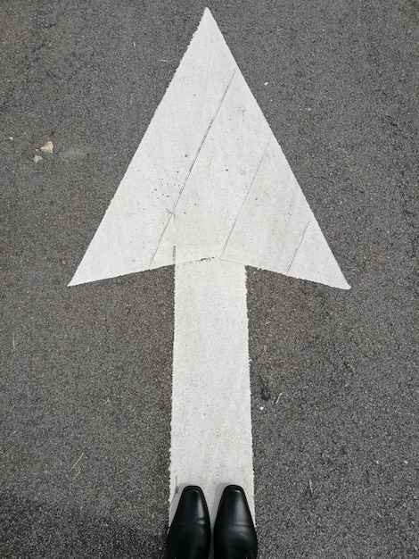 Foto vista de ângulo alto de sapatos por símbolo de flecha na estrada