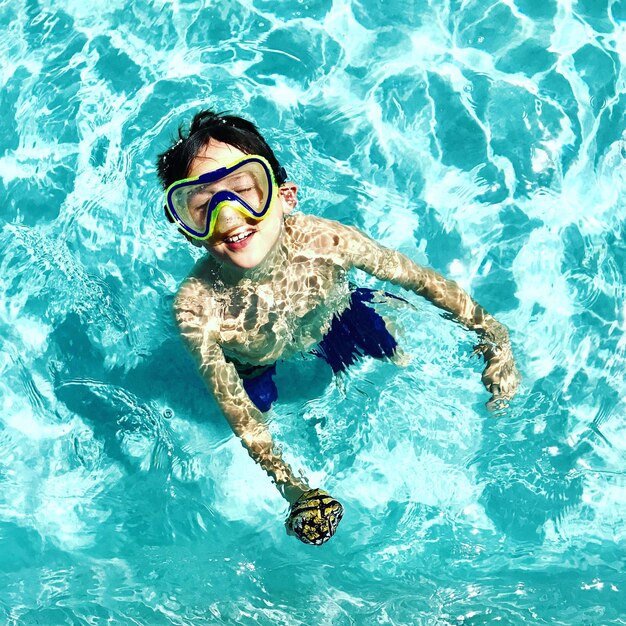 Foto vista de ângulo alto de um menino usando óculos de natação de pé na piscina