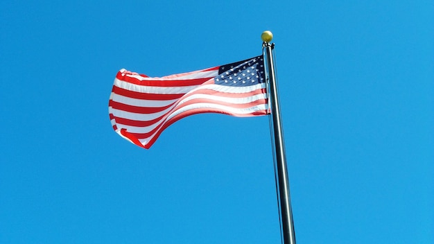 Vista de ângulo baixo da bandeira americana ondulando contra o céu azul claro