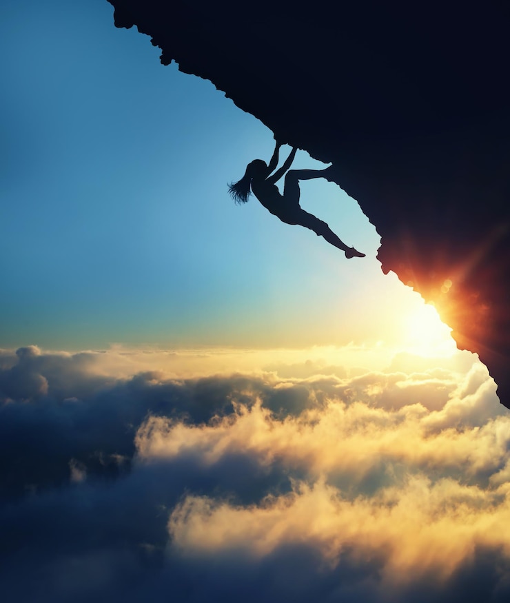 Foto vista de ângulo baixo da silhueta de uma mulher escalando uma montanha contra o céu durante o pôr do sol