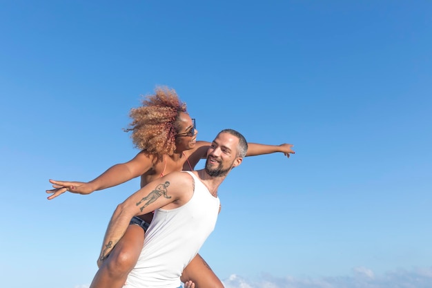 Vista de ângulo baixo de homem piggybacking namorada alegre contra o céu azul