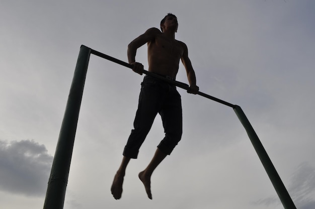 Vista de ângulo baixo de homem sem camisa realizando acrobacias contra o céu