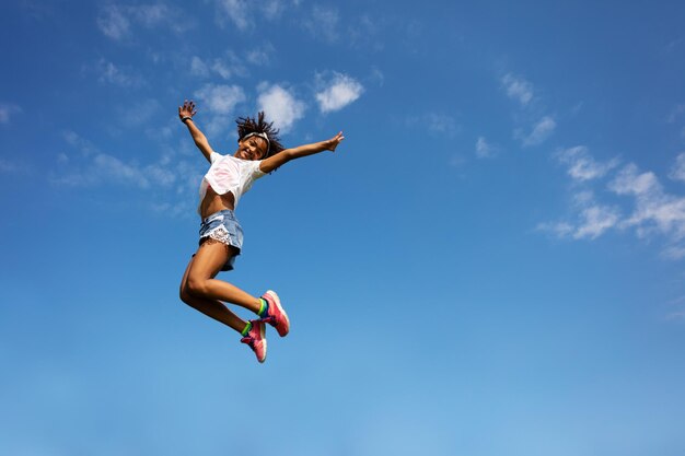 Foto vista de ângulo baixo de menina pulando contra o céu azul