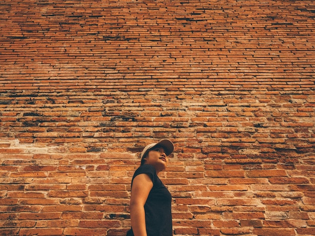 Foto vista de ângulo baixo de mulher de pé junto à parede de tijolos