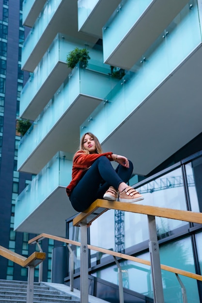 Foto vista de ângulo baixo de mulher sentada em um corrimão contra um edifício na cidade