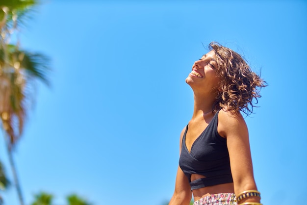 Vista de ângulo baixo de mulher sorridente desfrutando contra o céu azul claro