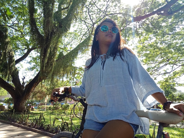 Foto vista de ângulo baixo de mulher usando óculos de sol em bicicleta contra árvores