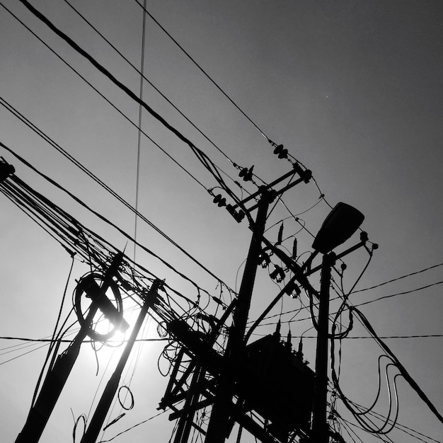 Foto vista de ângulo baixo de pilares elétricos em silhueta contra um céu claro