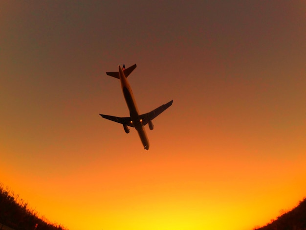 Foto vista de ângulo baixo de um avião de silhueta contra um céu claro durante o pôr-do-sol