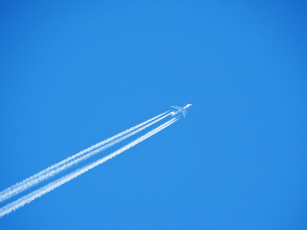 Foto vista de ângulo baixo de um avião voando contra um céu azul claro