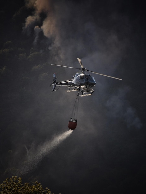 Vista de ângulo baixo de um helicóptero voando no céu lutando contra incêndios florestais