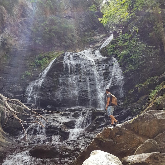 Foto vista de ângulo baixo de um homem de pé contra uma cachoeira na montanha