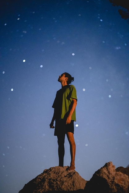 Foto vista de ângulo baixo de um homem de pé em uma rocha contra o céu noturno